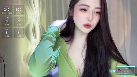 Media: Video of a young East Asian woman with long black hair, fair skin, and full lips, wearing a green top, adjusting her earrings. Background shows a virtual livestream with stats and viewers.