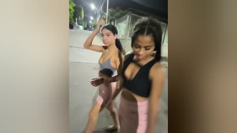 Media: Video of two women in tight athletic gear, one with medium breasts and the other with larger breasts, walking outdoors at night.