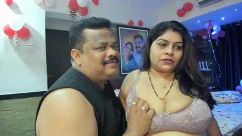 Media: Video of a smiling, overweight South Asian man with a mustache in a black tank top, standing next to a curvy, medium-skinned woman with long dark hair in a lavender bra.