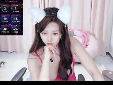 Media: A video of an East Asian woman with long dark hair and light skin, wearing a pink spaghetti-strap top, white cat ears, and a Bluetooth headset. She sits on a white chair in a pink room with a stuffed animal.