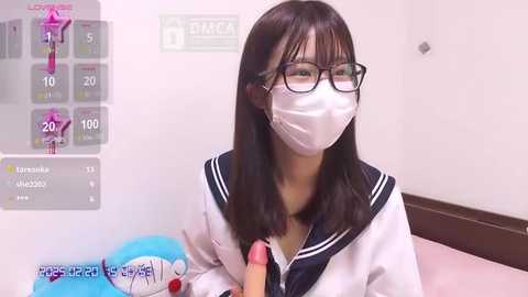 Media: A video of a young East Asian woman in a school uniform, wearing glasses and a mask, holding a dildo. The setting appears to be a hospital room with a chart displaying temperature and pulse readings.