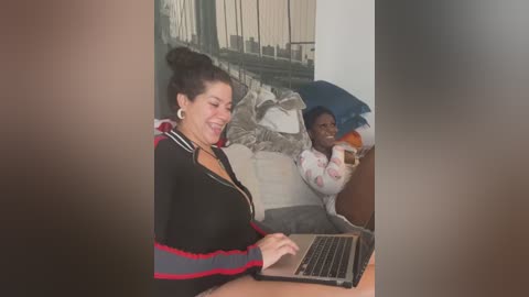 Media: A video captures a woman in a black jacket with red stripes and a man in a white shirt and red pajama pants sitting on a couch, both smiling.