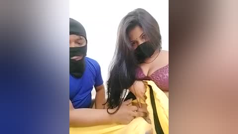 Media: Video of a woman with long black hair, wearing a black mask and purple lace bra, being held by a man in a blue shirt and black mask.