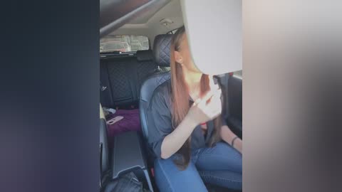 Media: A video of a woman with long, straight brown hair, wearing a black sweater and blue jeans, sitting in the back seat of a car, partially obscured by her hair.