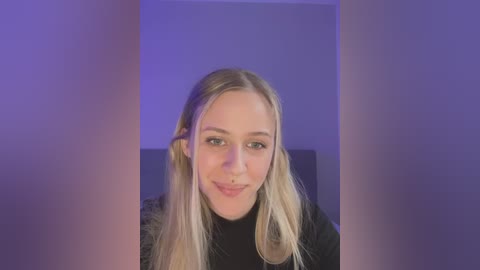 Media: A video of a young Caucasian woman with long, straight blonde hair, fair skin, and blue eyes, smiling slightly. She wears a black top. Background features a soft purple glow and a plain, light-colored wall.