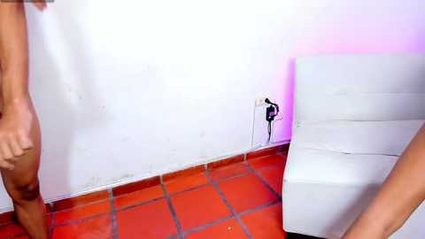 Media: Video of a white toilet and tiled floor in a dimly lit bathroom with pink lighting, showing a man's lower legs and genitals standing near the toilet.