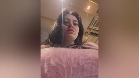 Media: Video of a young woman with long, dark hair, wearing a fuzzy pink sweater, leaning against a mirror, capturing her reflection and surroundings.