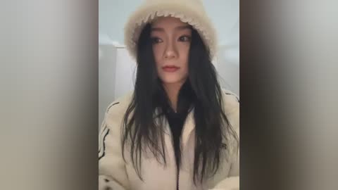 Media: A video of an Asian woman with long black hair, wearing a white beanie and a cream-colored jacket, standing against a blurred white background.