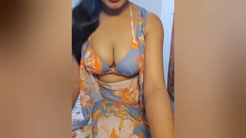 Media: A video of a woman in a blue floral dress with a plunging neckline, revealing ample cleavage, and a sheer orange scarf draped over her shoulders.