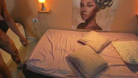 Media: Video of a beige-tiled bedroom with a neatly made bed featuring a cream-colored pillow and a textured beige blanket. A woman, partially visible, stands in the background, wearing a black top. A large portrait of a Black woman with an afro hangs on the wall.