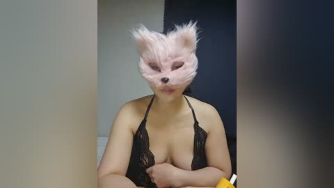 Media: Video of a woman in a black lace bra, wearing a pink bear mask, with a blurred background.