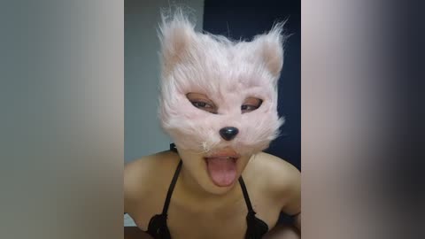 Media: Video of a person with a white, fluffy wolf mask, tongue out, wearing a black strapless bra, against a dark background.