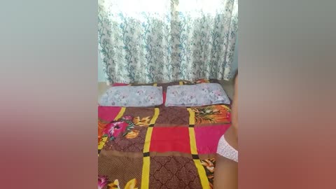 Media: Video of a cozy bedroom with a floral-patterned quilted bedspread, floral curtains, and a white pillow, bathed in natural light.