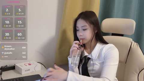 Media: Video of an Asian woman in a white lab coat, sitting at a desk with a digital screen displaying medical data, sipping water, in a modern, clinical setting.