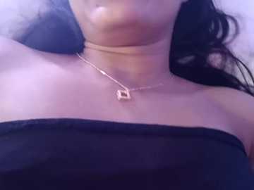 Media: Video of a woman with medium brown skin, wearing a black strapless dress, a gold necklace with a square pendant, and long dark hair.