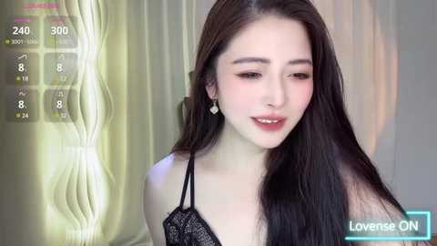 Media: Video of a young, fair-skinned Asian woman with long black hair, wearing a black lace bralette, smiling softly, against a backdrop of white curtains.