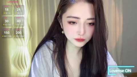 Media: Video of a young East Asian woman with long, straight black hair, fair skin, and delicate facial features, wearing a white robe, against a blurred beige background.