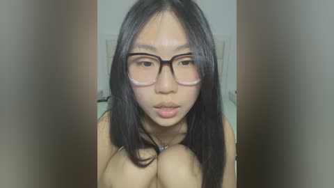 Media: Video of an Asian woman with straight black hair, wearing glasses, topless, showing cleavage, indoors, blurred background.