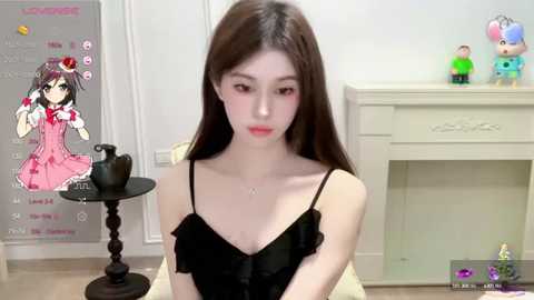 Media: A video of an Asian woman with long brown hair, wearing a black dress, sitting in a room with white walls and a beige fireplace.