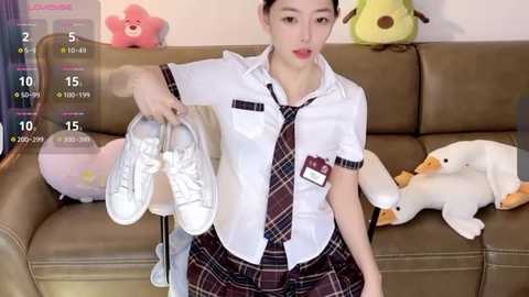 Media: A video of a young Asian woman in a white blouse, plaid skirt, and black tie, holding white sneakers, sitting on a brown couch with plush toys.