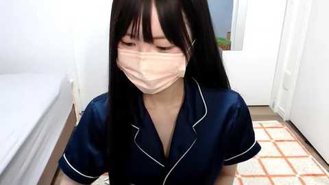 Media: Video of an East Asian woman with long black hair, wearing a navy blue satin robe with white trim, a beige face mask, and a white door in the background.