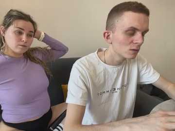 Media: Video of a young Caucasian couple, the woman with long brown hair in a lavender top, the man with short brown hair in a white shirt, sitting in a dimly lit room.