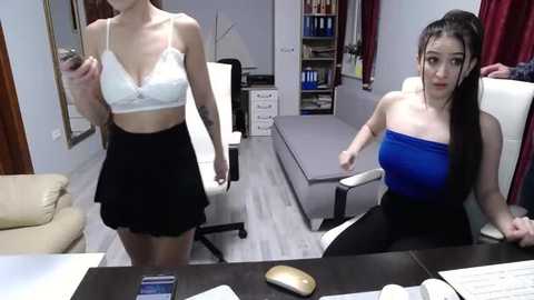 Media: Video of two Asian women in a modern office: one in a white lace bra and black skirt, the other in a blue tube top and black pants.