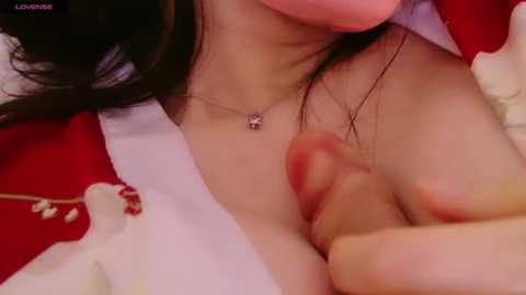 Media: A close-up video of an Asian woman with fair skin, black hair, and a silver necklace, sucking on a penis, revealing her bare breasts with small nipples. She wears a red and white robe.