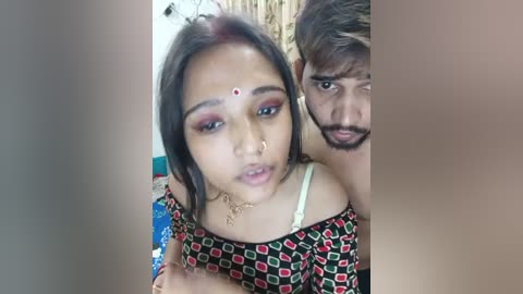 Media: Video of a young woman with a bindi, wearing a patterned top, and a man with a beard, both smiling, in an indoor setting.