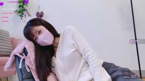 Media: A video of an Asian woman with long black hair, wearing a pink face mask, lying on a bed in a room with pink heart decorations.