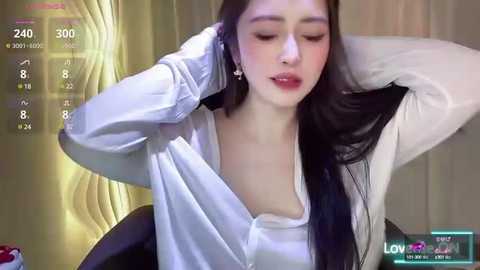 Media: Video of an Asian woman with long black hair, wearing a white shirt and a black cardigan, adjusting her hair. Background features a computer screen displaying live stream information.