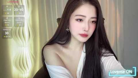 Media: A video of a young East Asian woman with long, straight black hair, fair skin, and a petite frame, wearing a white off-shoulder blouse, standing against a soft, greenish-yellow backdrop.