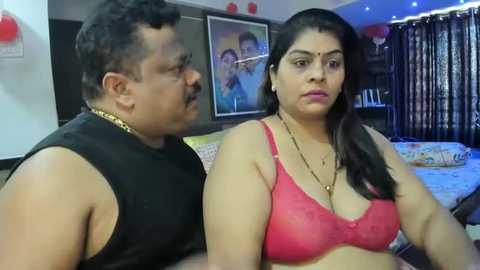 Media: Video of a South Asian couple in a bedroom; man in black sleeveless shirt, woman in red lace bra, both looking serious.