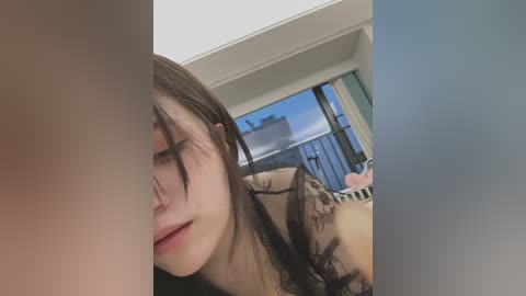 Media: Video of a young woman with long brown hair, light skin, and closed eyes, resting her head on a pillow. Background shows a window with a cityscape view.