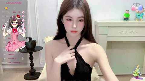 Media: Video of a young Asian woman with fair skin, long brown hair, and red lipstick, wearing a black halter dress, sitting in a bright room with a white dresser and colorful toys.