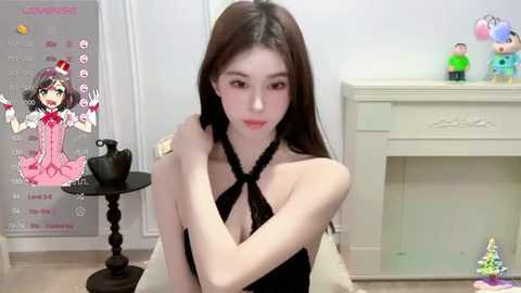 Media: Video of a young Asian woman with long black hair, wearing a black halter dress, posing in a room with a white fireplace, colorful toys, and a calendar on the wall.