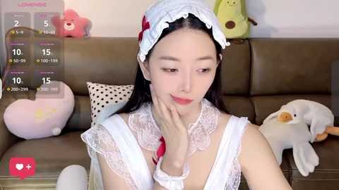 Media: A video of a young East Asian woman with long black hair and pale skin wearing a white lace headband and nurse costume, seated on a brown couch.