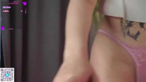 Media: A video of a woman's side profile showing a tattoo, wearing pink lace panties. The background is blurred, with digital icons and text on the left.