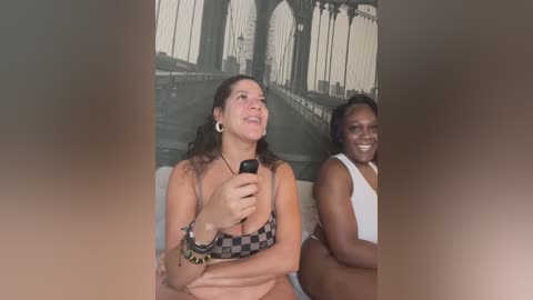 Media: A candid video of two women seated, one holding a phone, the other smiling. Background features a mural of the Brooklyn Bridge.