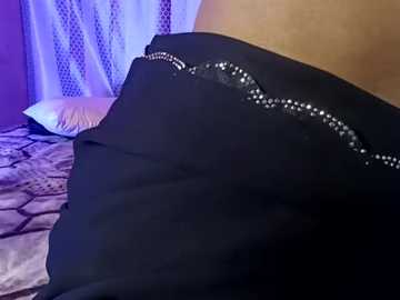 Media: Video of a black satin bedspread with a decorative silver beaded trim, featuring a white pillow and a beige wall in the background.