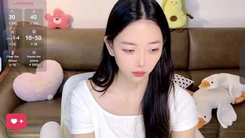 Media: A video of an East Asian woman with long black hair, fair skin, and red lipstick, sitting on a brown leather couch with stuffed toys.