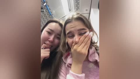 Media: A video of two young women in a bathroom, one with long hair, the other with short hair, both wearing pink robes, covering their faces with hands, and smiling.