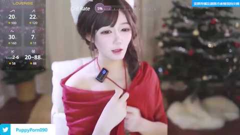 Media: Video of a fair-skinned woman with brown hair, wearing a red dress, holding a fitness tracker, in a cozy room with a Christmas tree in the background.