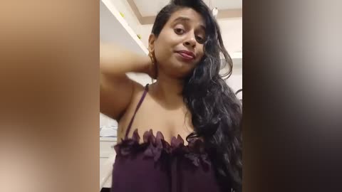 Media: A video of a South Asian woman with long black hair, medium brown skin, and wearing a purple lace-trimmed camisole, taken in a dimly lit bathroom with blurred toilet paper rolls in the background.