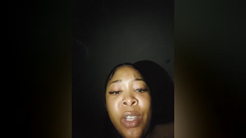 Media: Video of a young African-American woman with light brown skin, wearing minimal makeup, and a toothy grin, against a dark, blurry background.