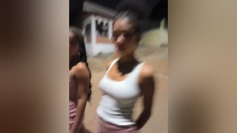 Media: Video of two African-American women outdoors, one with braids and a white tank top, the other in a pink dress. Background shows a blurred house.