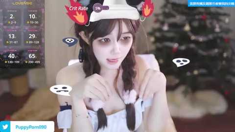 Media: A video of a young woman with long black hair, wearing a white furry hat with flames, a white fur collar, and a smile. She's in a cozy room with a decorated Christmas tree in the background.