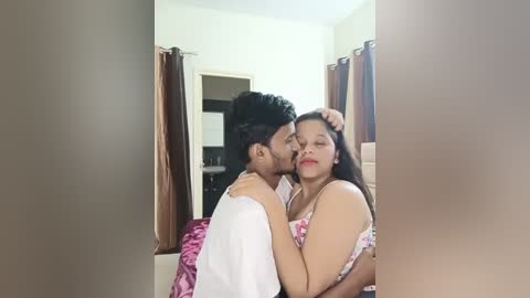 Media: Video of a South Asian couple in a dimly lit room, embracing passionately. The woman, with long dark hair and fair skin, wears a pink dress, while the man, with short black hair and medium brown skin, is shirtless.