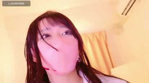 Media: A video of an Asian woman with long, wet hair, giving a close-up selfie. She has a fair complexion and is in a bathroom with a beige shower curtain. The image is slightly out of focus.