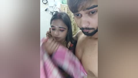 Media: A blurry video of a young South Asian woman with pink eye makeup and a man with a beard, both topless, in a bathroom with a pink towel.